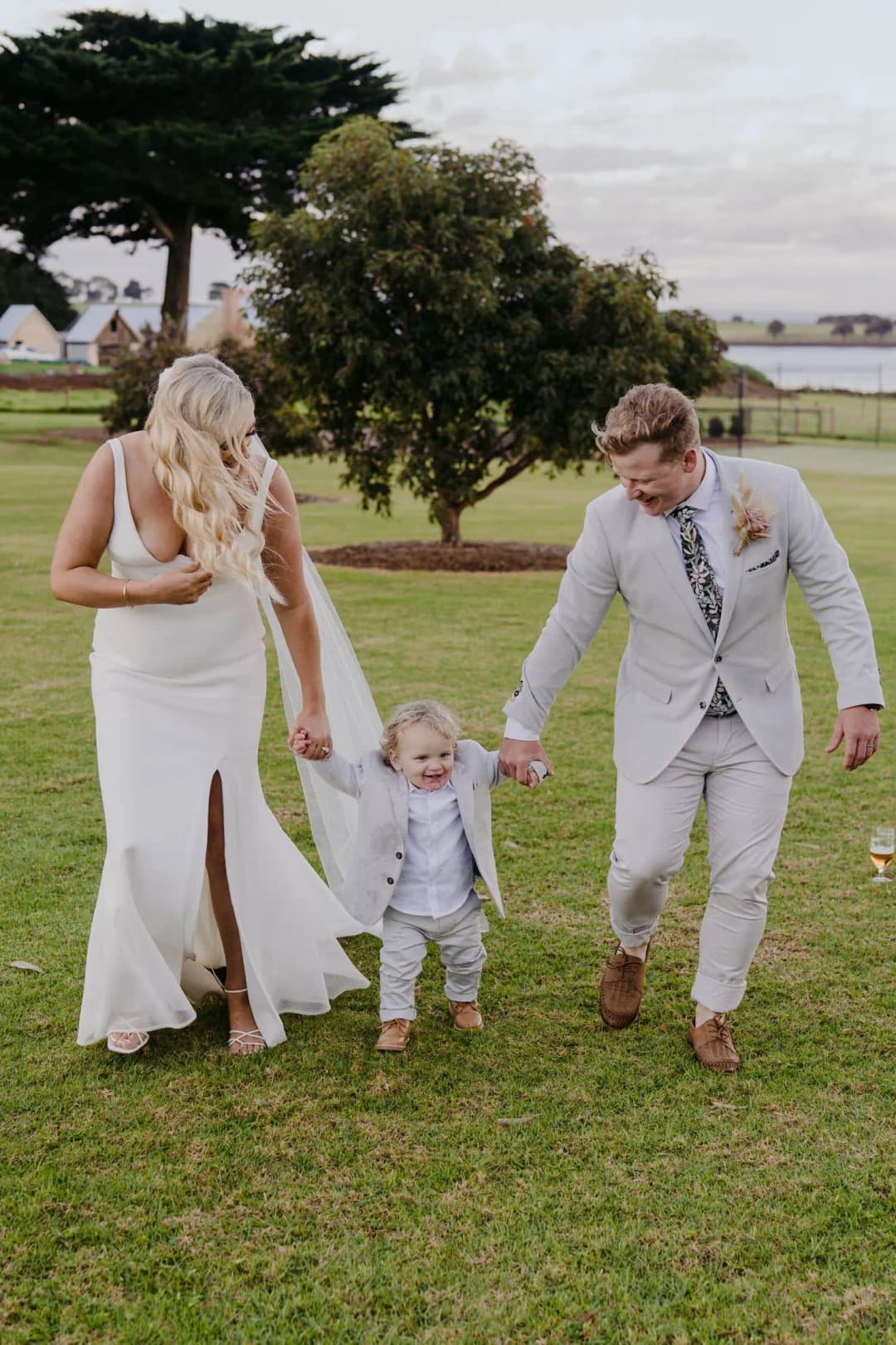 Bride and groom holding a small child’s hands as they walk on the lawn