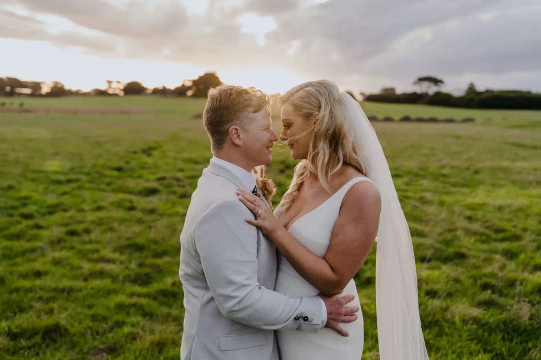 Newlyweds holding each other in a green paddock as the sun sets