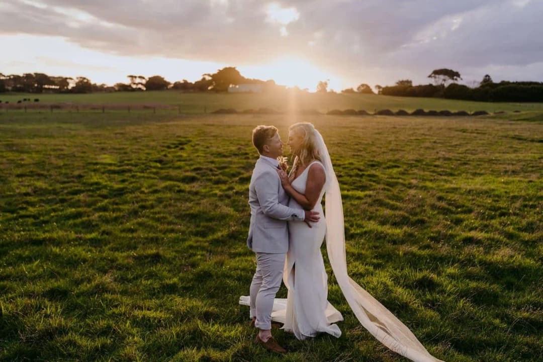 Bride and groom embracing in a paddock beneath a glowing sunset