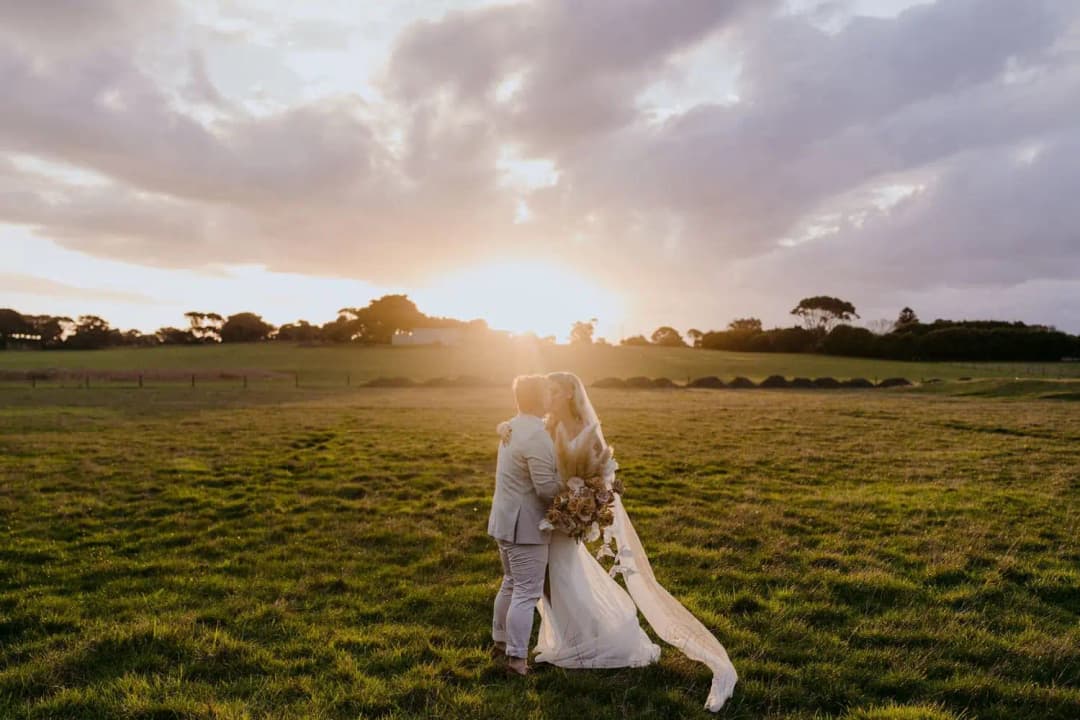 Newlyweds embracing on a green lawn beneath a colourful sunset