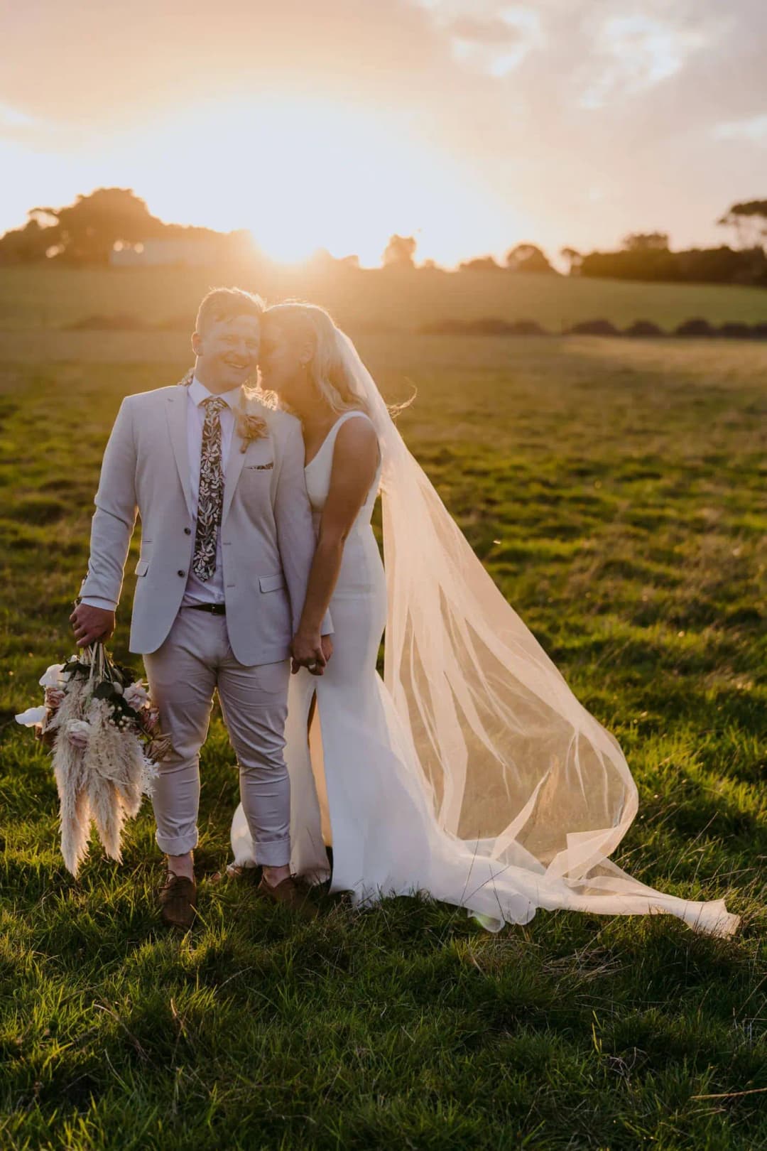 Bride and groom standing together with a flowing veil in the evening sunlight