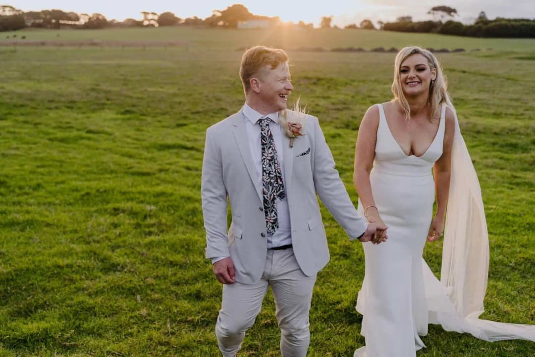 Newlyweds laughing and walking hand in hand across the paddock