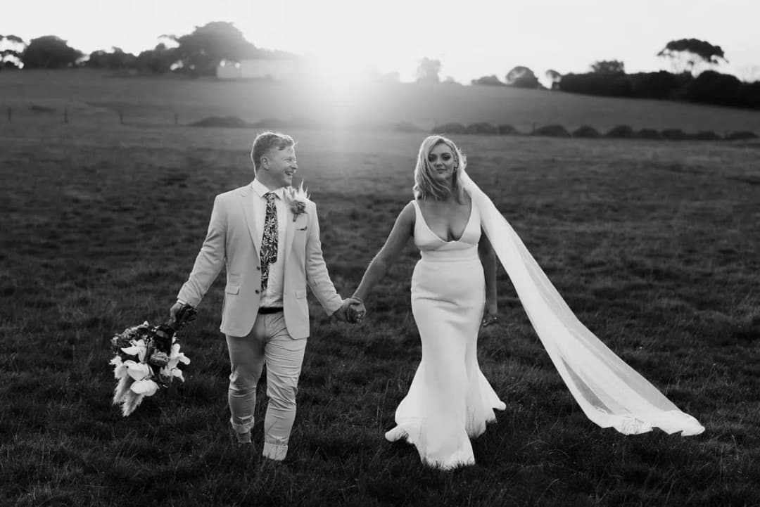 Black-and-white photograph of newlyweds walking with their bouquet and flowing veil