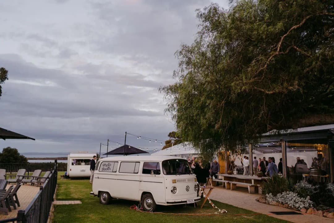White caravan bar beside guests and trees as evening falls