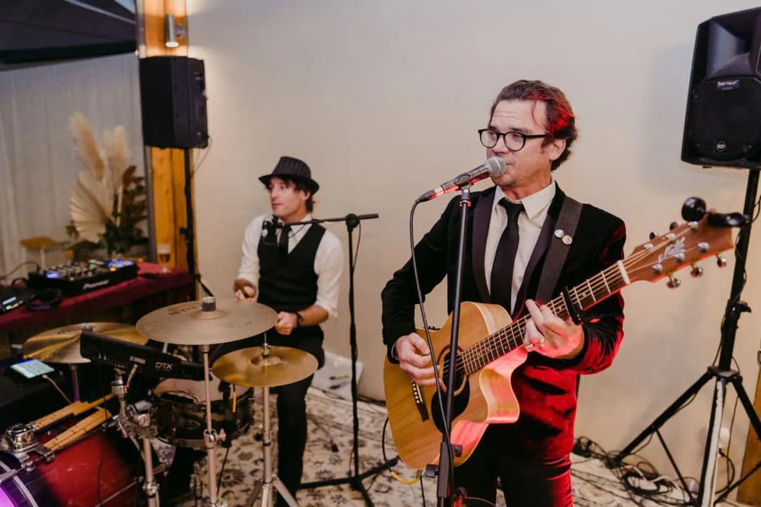 Singer with an acoustic guitar performing beside a drummer