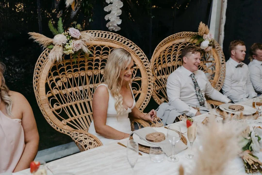 Bride and groom smiling from wicker chairs at the wedding table