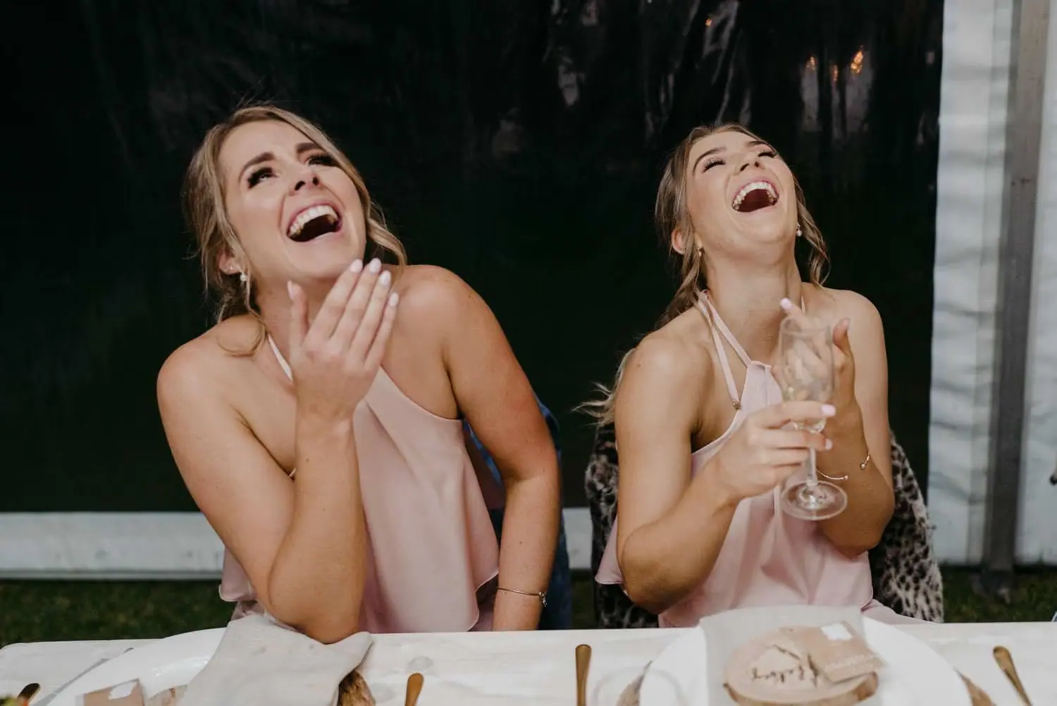Two bridesmaids laughing together while seated at the wedding table