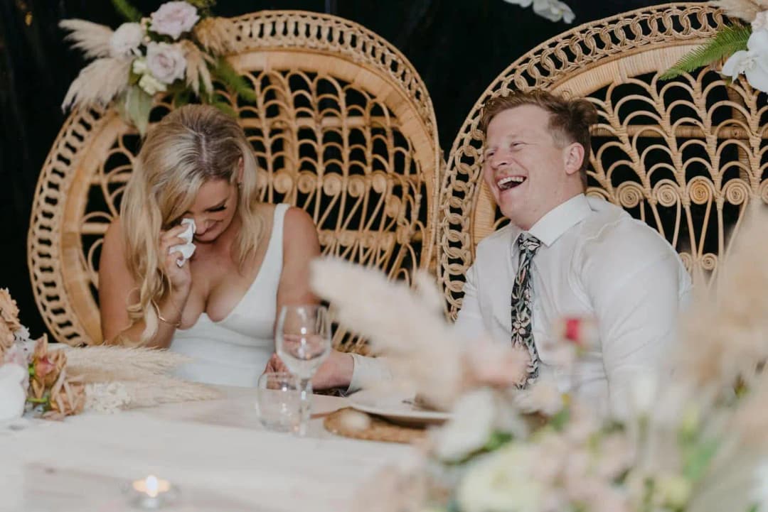 Bride and groom laughing while seated at the reception table