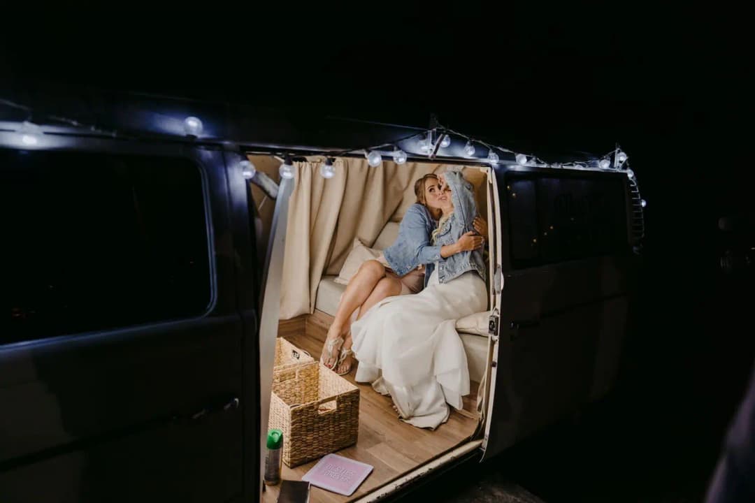 Bride seated inside a lit caravan at night wearing a denim jacket