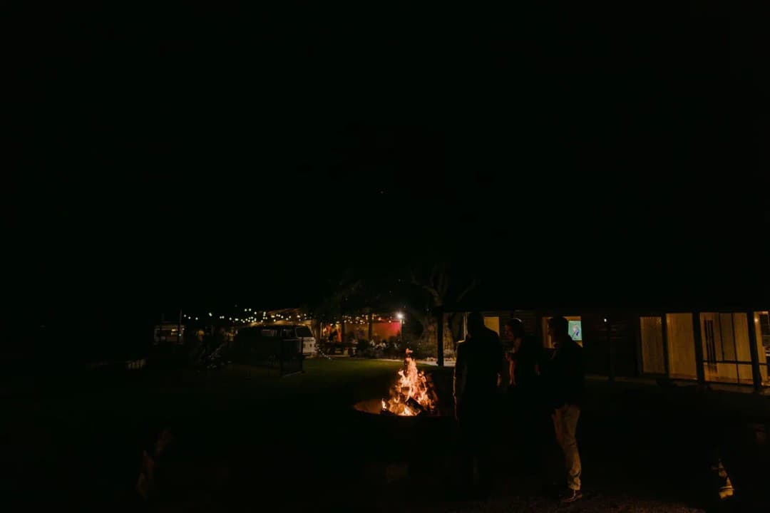 Guests gathered beside a glowing outdoor fire and lit reception buildings at night
