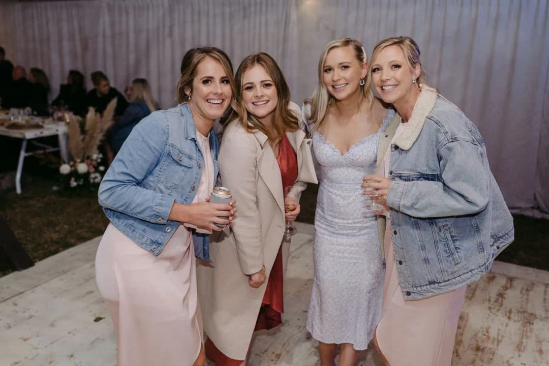 Bride and bridesmaids smiling together at the reception in denim jackets