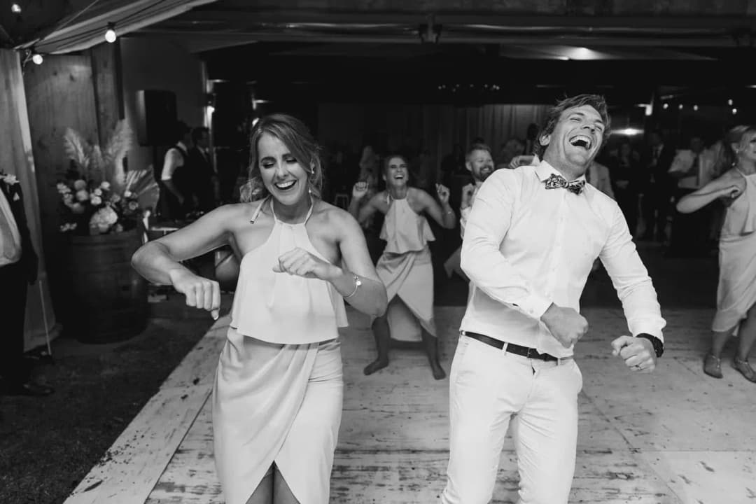 Black-and-white photograph of a guest and a groomsman dancing with wide smiles
