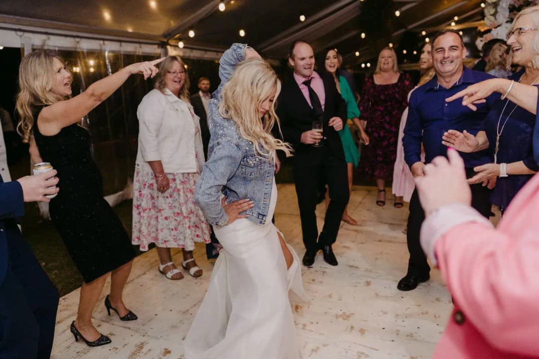 Bride laughing as guests dance around her at the reception