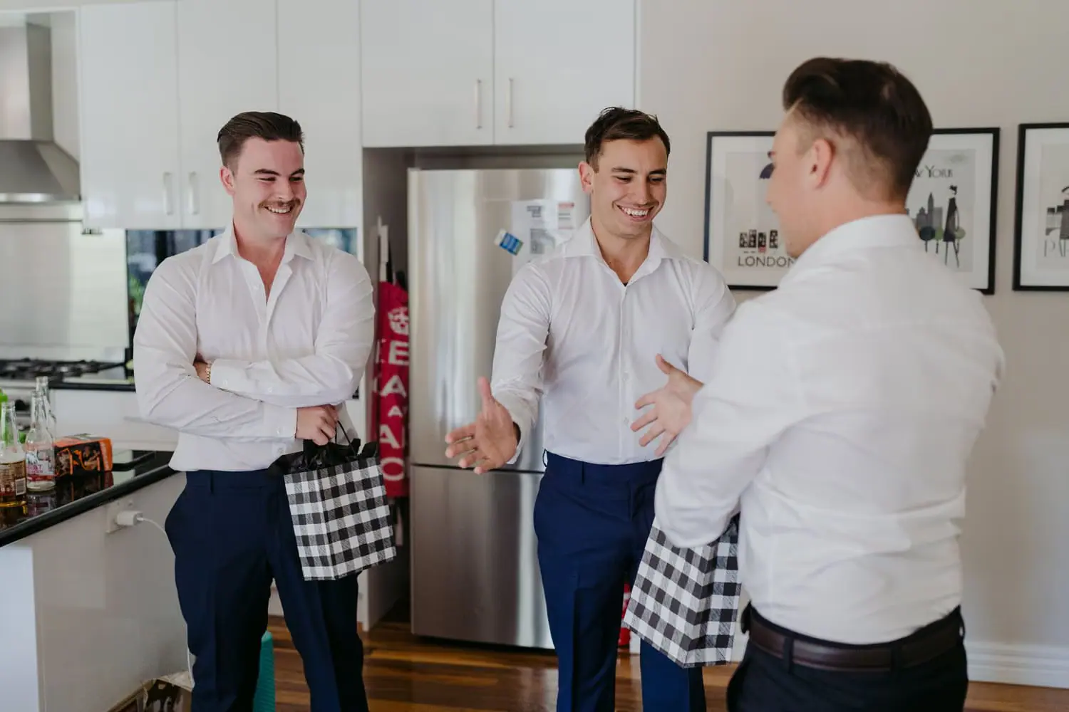 Three men in white shirts laughing together while getting ready in a kitchen