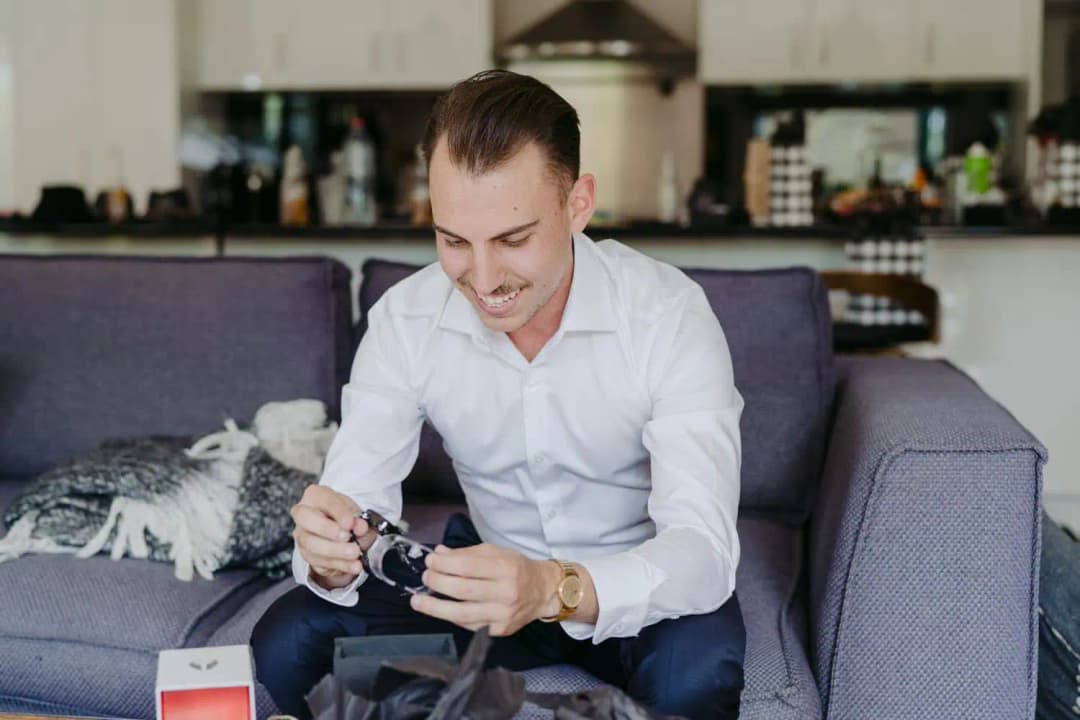 Groom smiling while looking at an item in his hands on a sofa