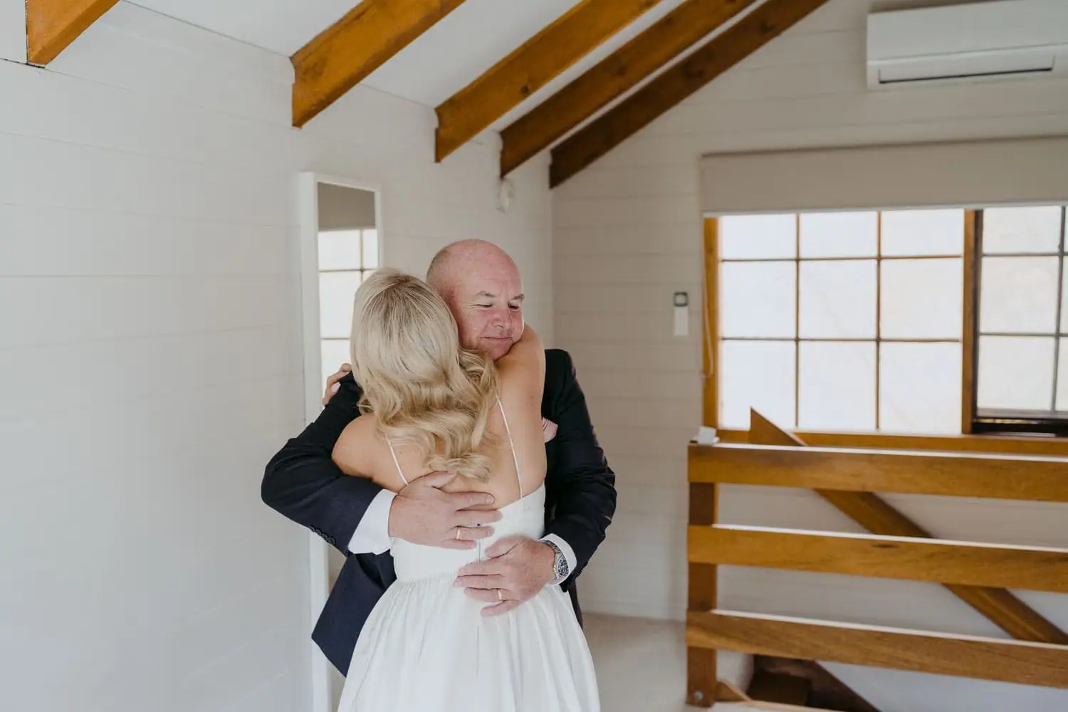 Bride embracing a bald man in a suit inside a bright room