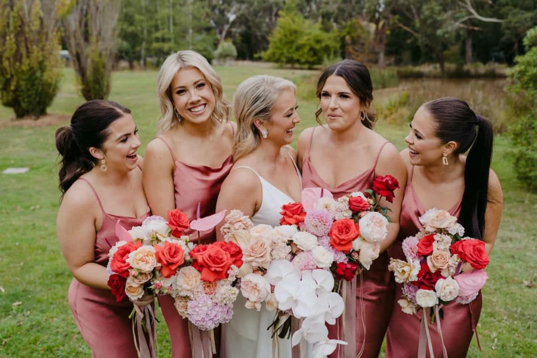 Bride and bridesmaids laughing together with pink, red and white bouquets