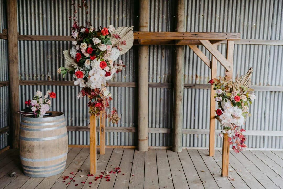 Timber ceremony arch decorated with red and white flowers inside a shed