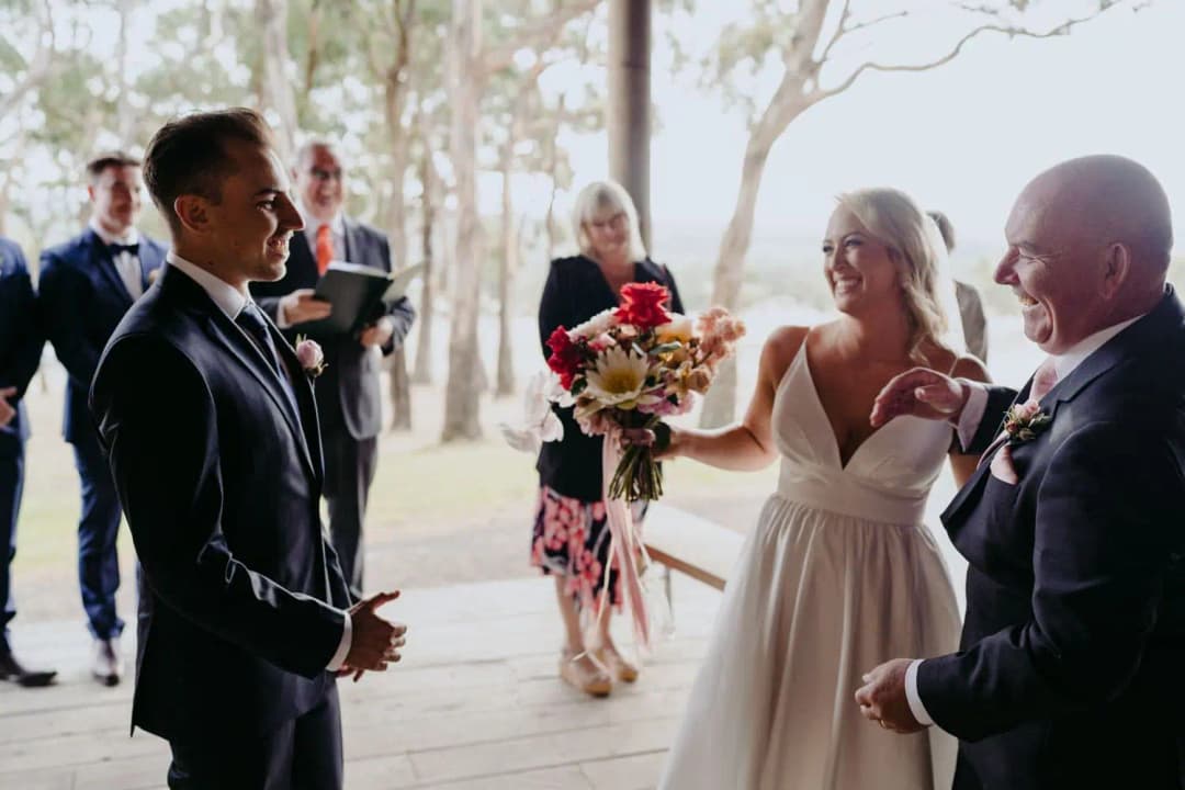 Bride smiling between the groom and a suited man at the start of the ceremony