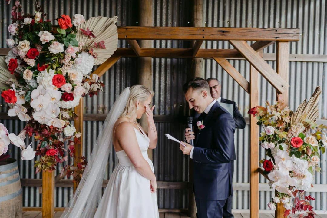 Groom reading into a microphone while the bride touches her face