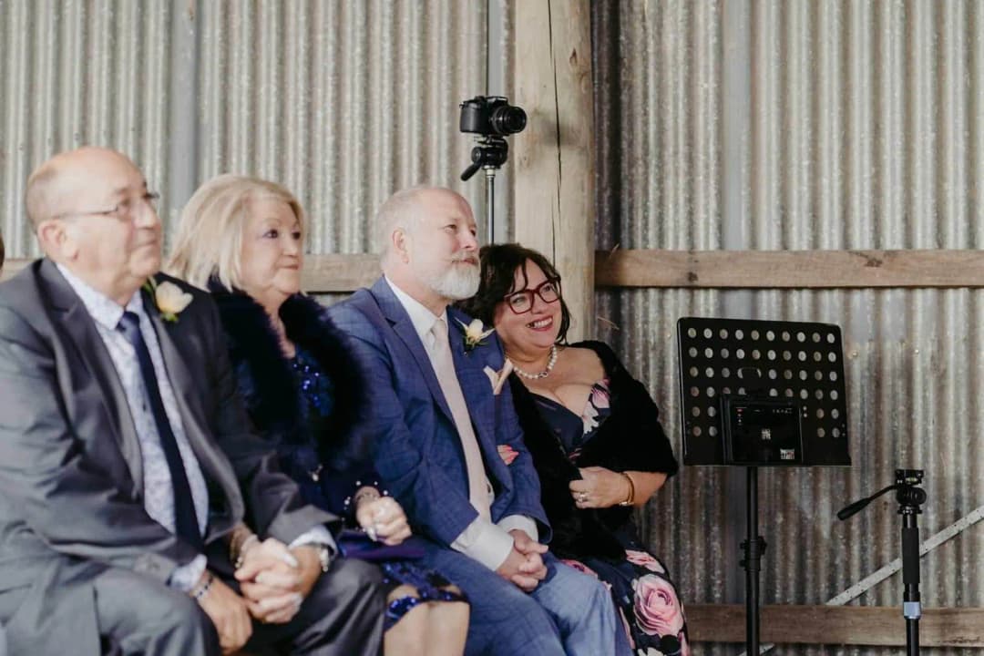 Four smiling guests seated beside the corrugated shed wall
