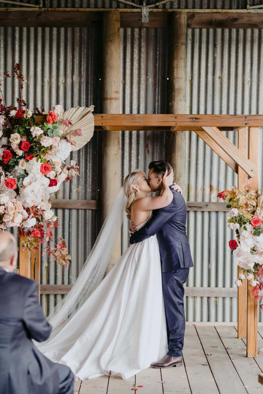 Bride and groom kissing beneath the timber floral arch
