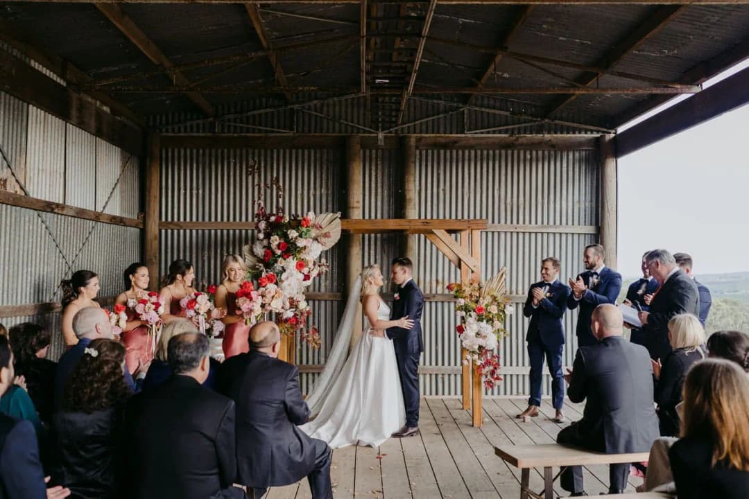 Wedding party applauding as the couple kiss beneath the shed roof