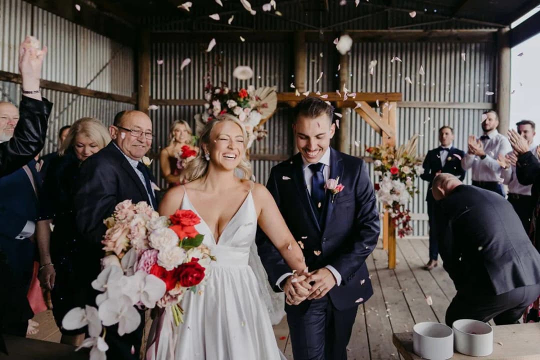 Bride and groom walking through falling petals as guests celebrate