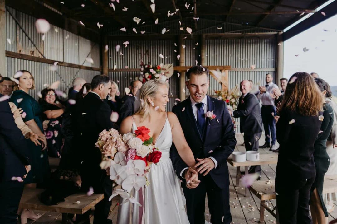 Bride and groom smiling at each other while walking beneath falling petals