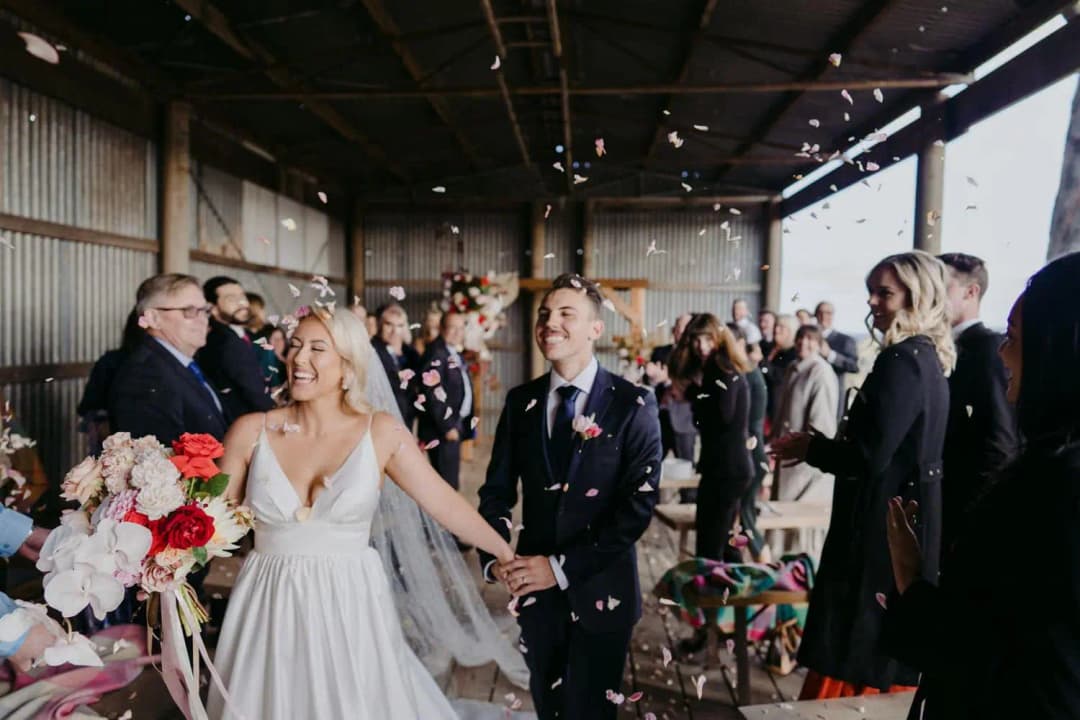 Bride and groom holding hands as guests toss petals along the aisle