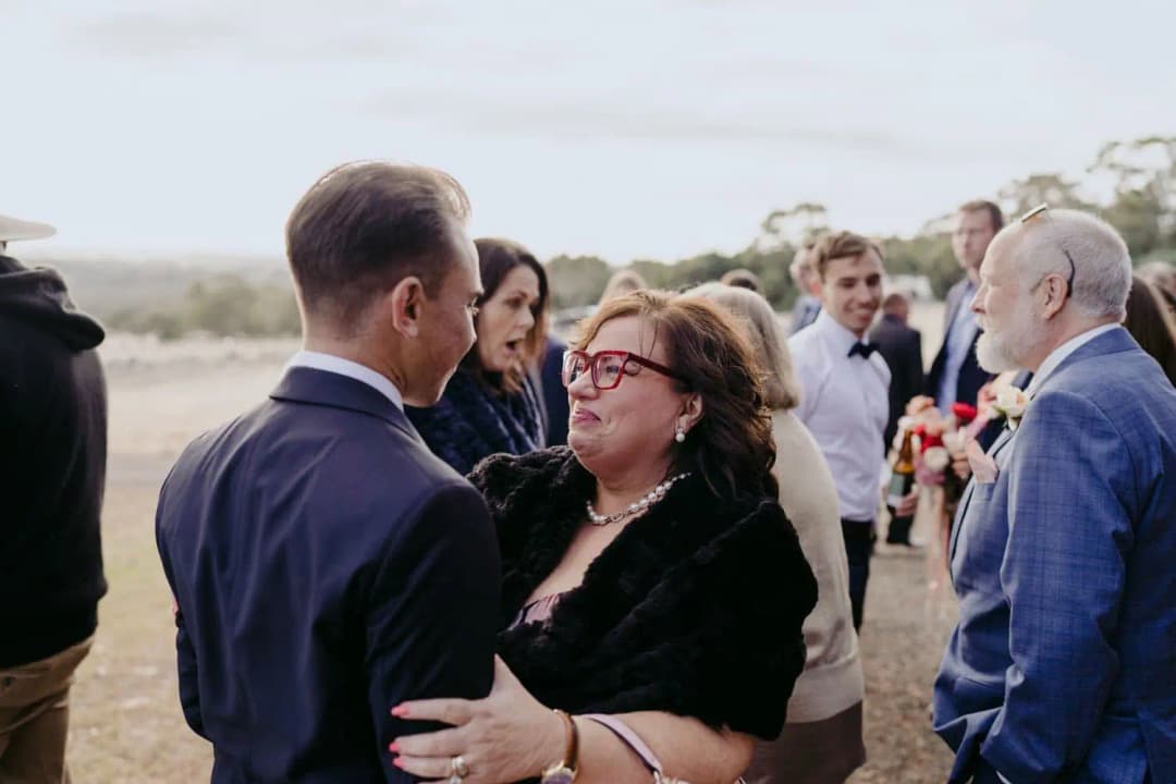 Groom greeting a guest in a dark wrap outside the ceremony shed