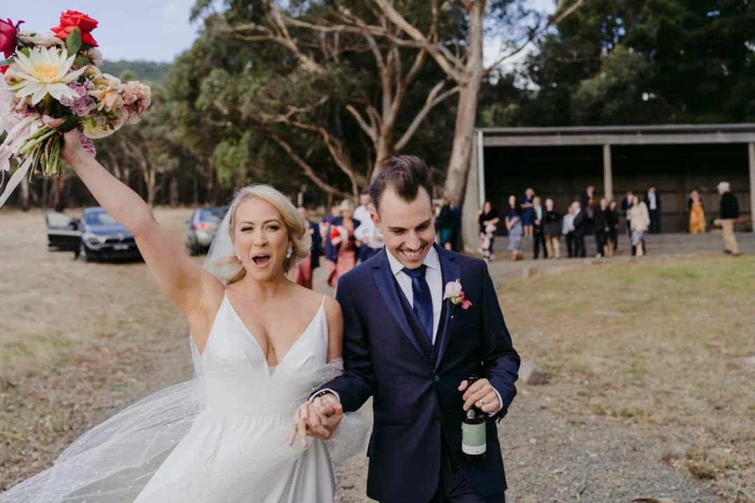 Bride raising her bouquet as she walks with the groom outside
