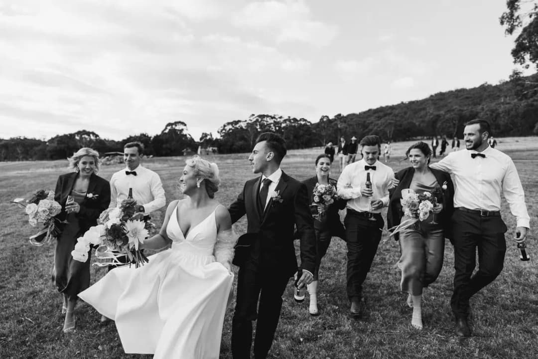 Black and white photograph of the couple laughing with their wedding party in a field