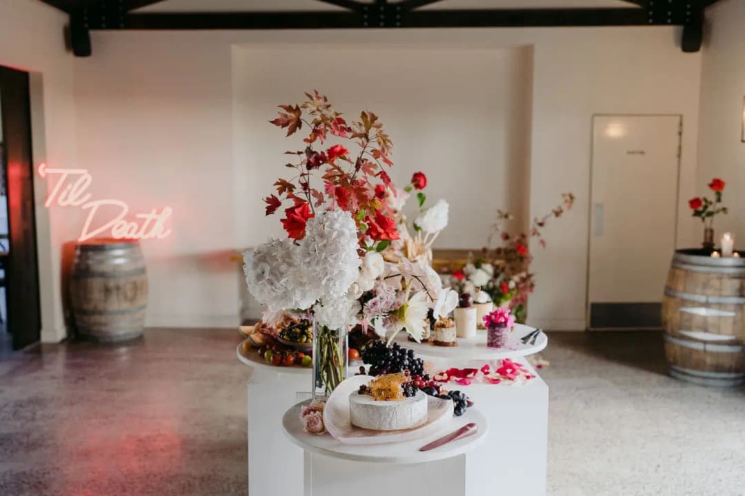 Reception display with cakes, fruit and red and white flowers on white stands