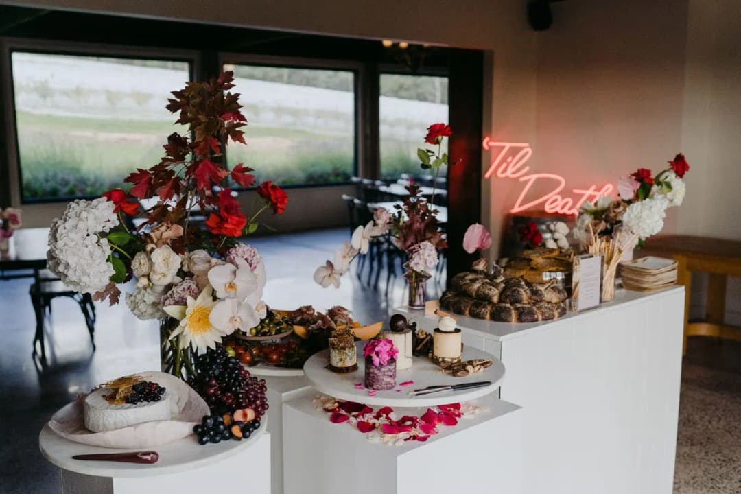 Floral arrangements and desserts displayed beside an illuminated Til Death sign
