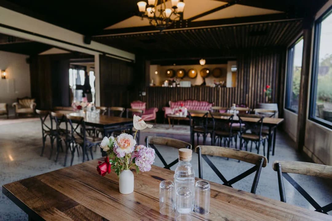 Wooden reception tables with flower arrangements beneath a timber roof
