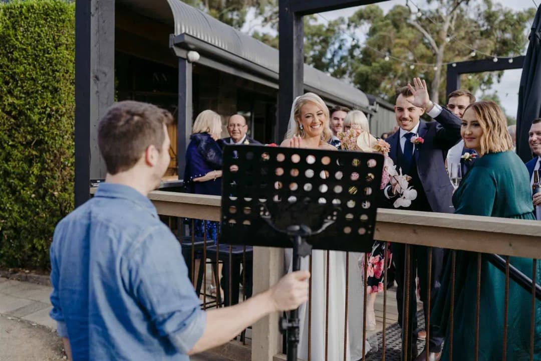 Guests smiling and raising drinks toward a man speaking beside a music stand