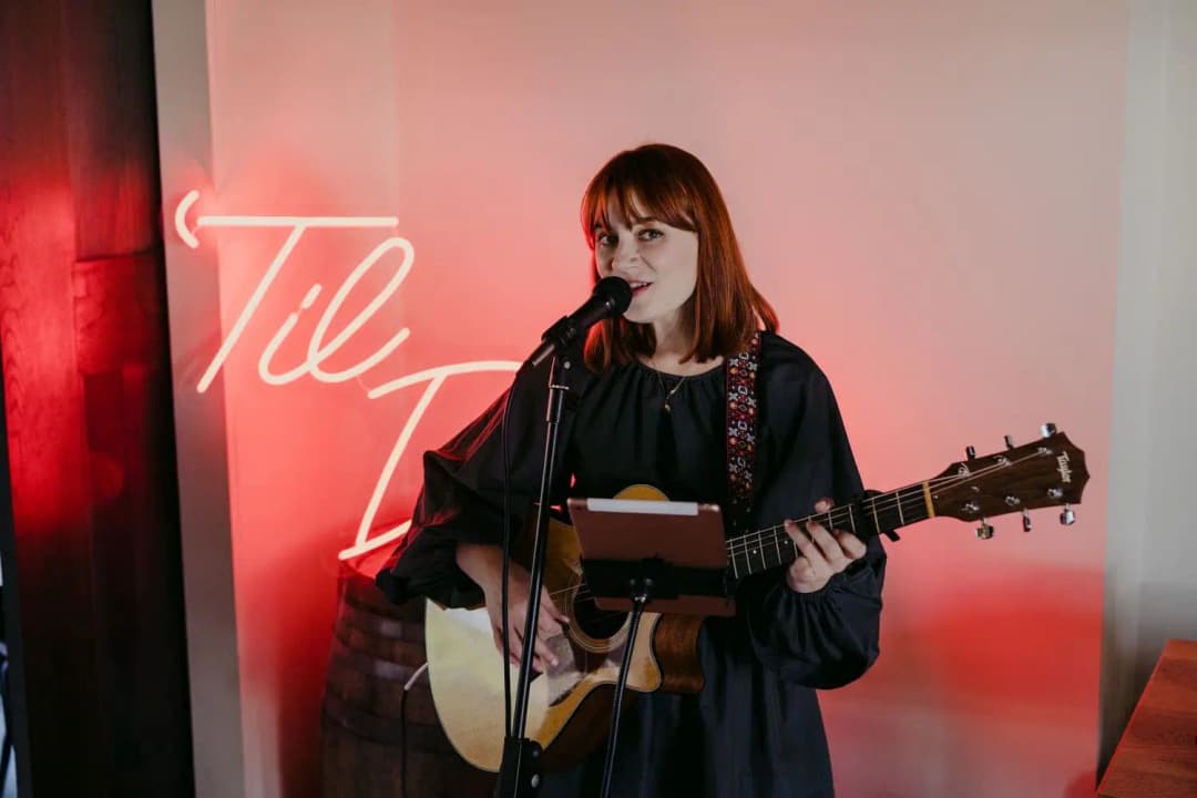 Singer playing an acoustic guitar beside an illuminated reception sign