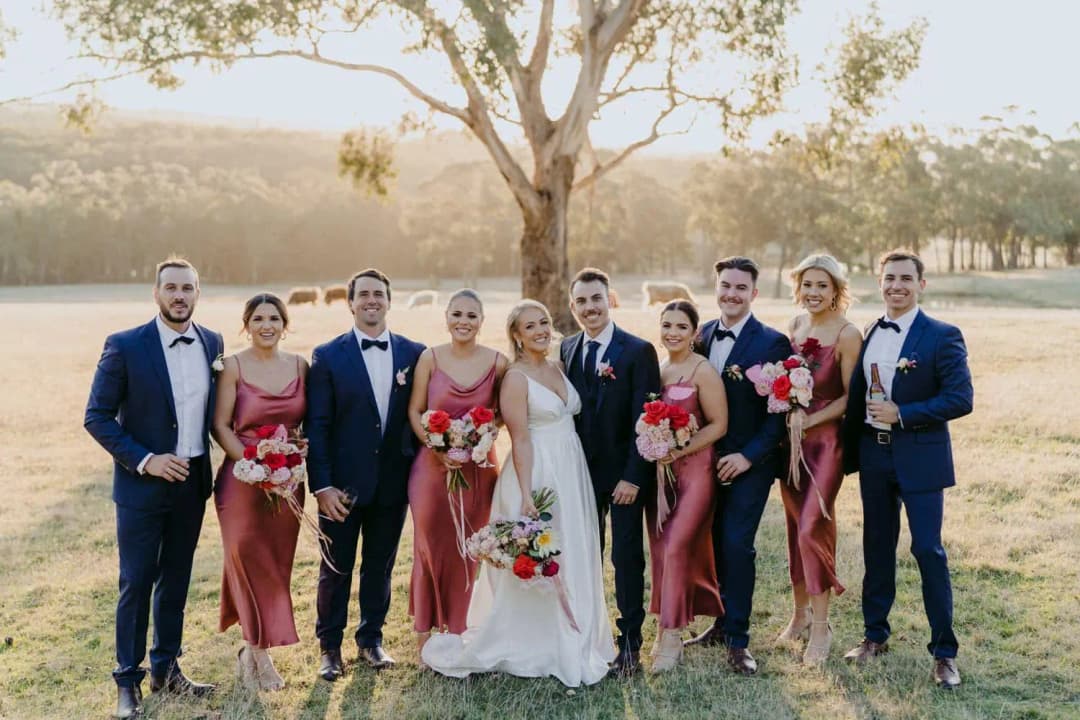 Wedding party posing together with bouquets beneath a tree