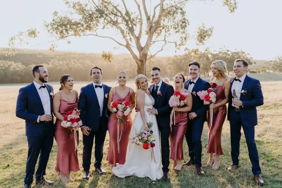 Wedding party laughing together in an open field beneath a tree