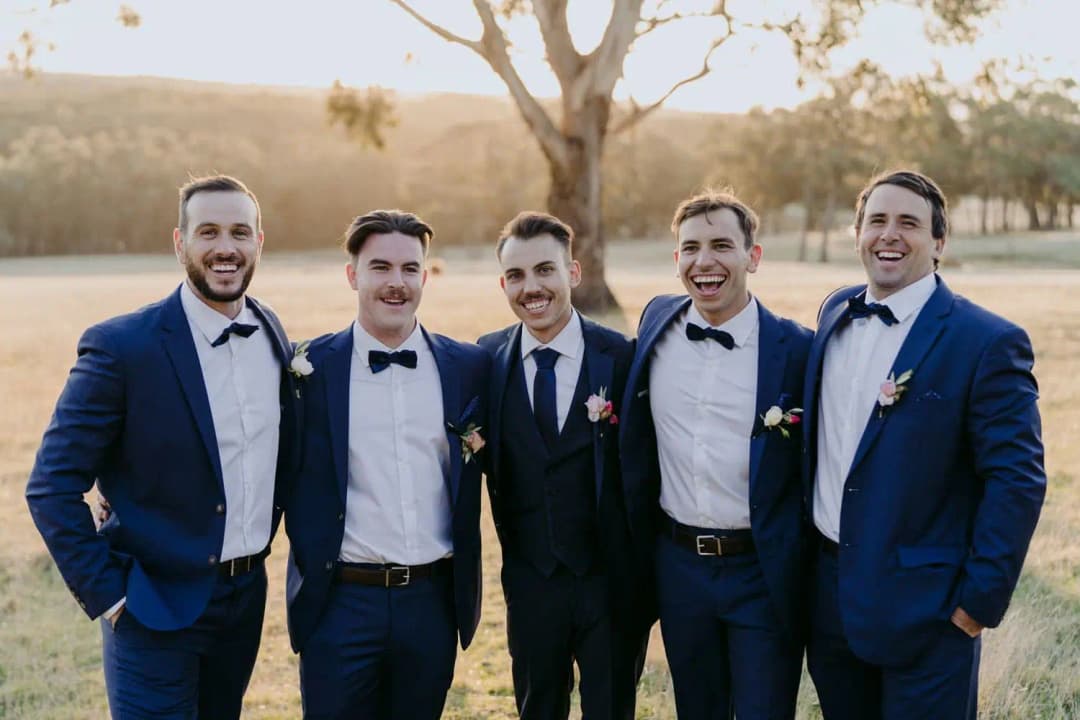 Five men in navy suits laughing together outdoors