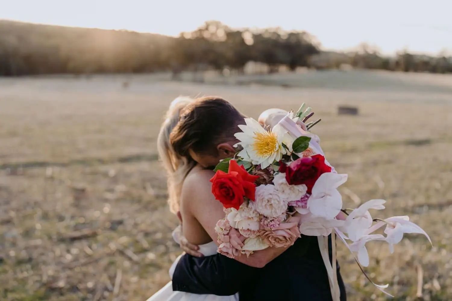 Bride and groom embracing with a colourful bouquet in the foreground