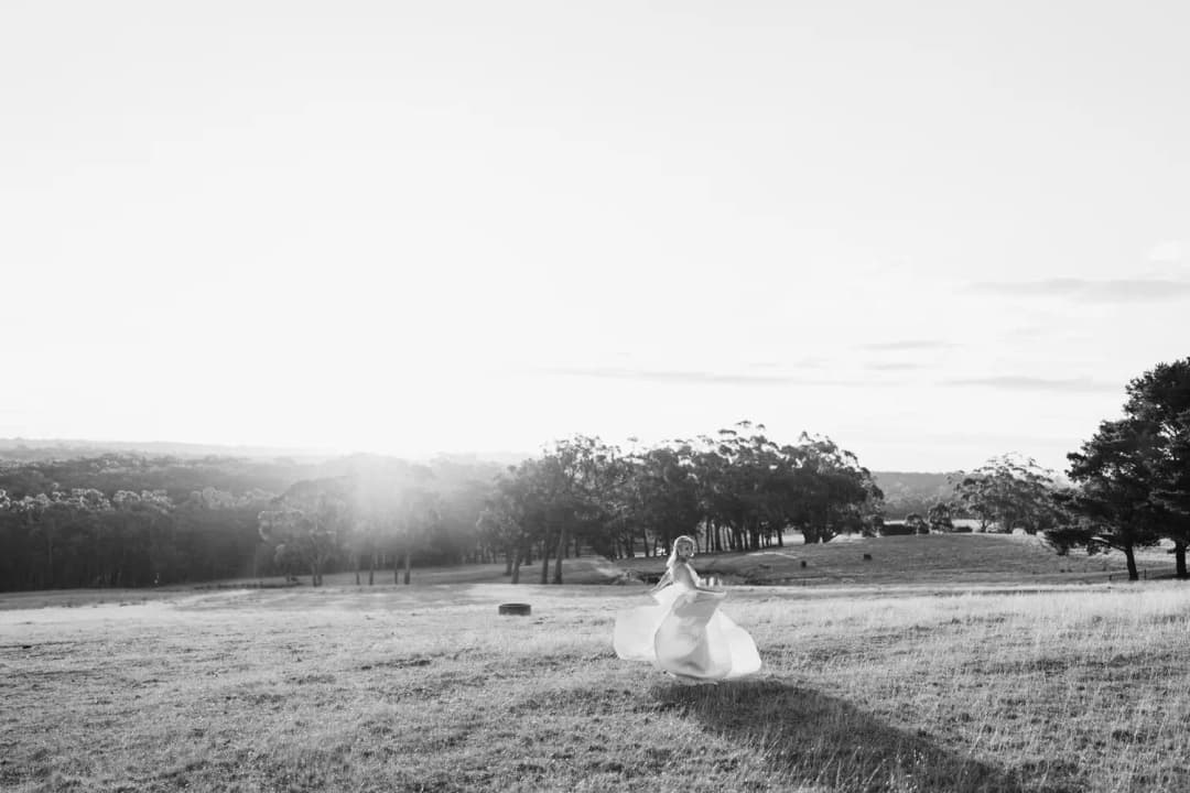 Wide black and white photograph of the bride spinning in a field at sunset