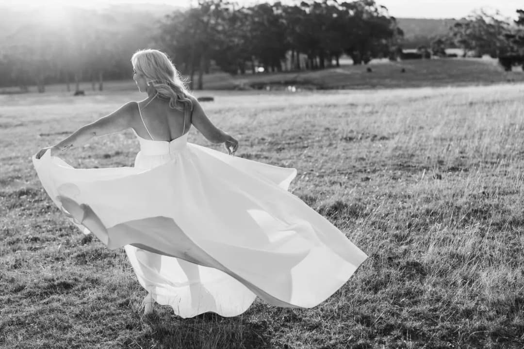 Black and white photograph of the bride holding out her flowing dress as she turns