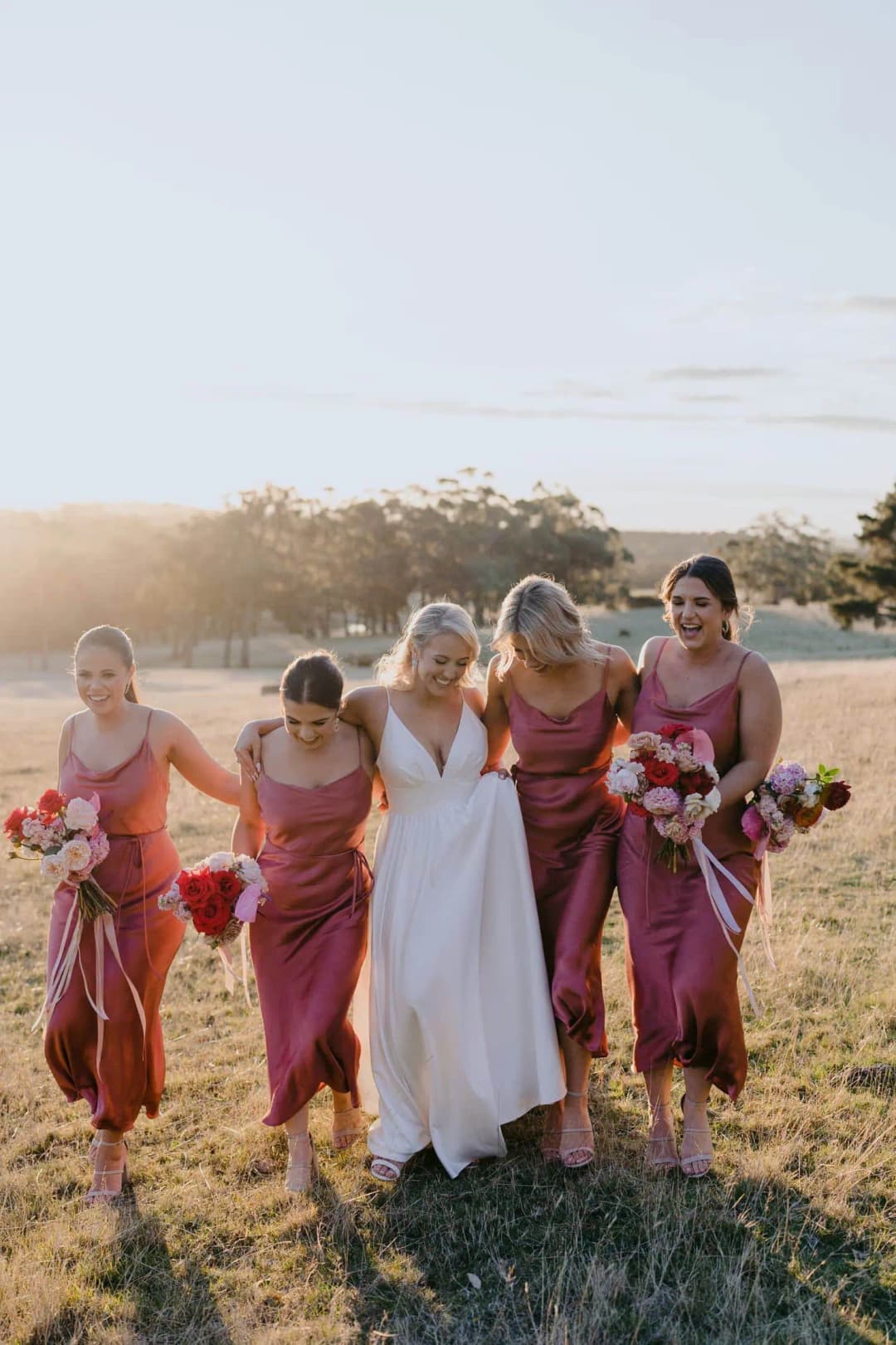 Bride and bridesmaids walking together across a sunlit field