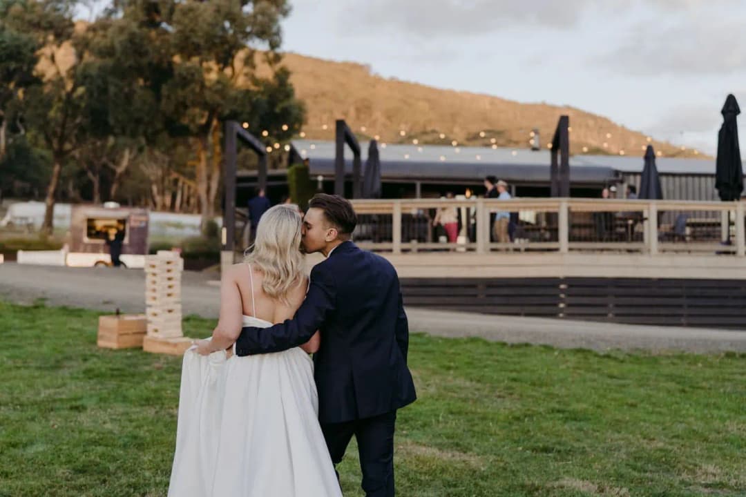 Groom kissing the bride's temple as they walk toward the reception deck