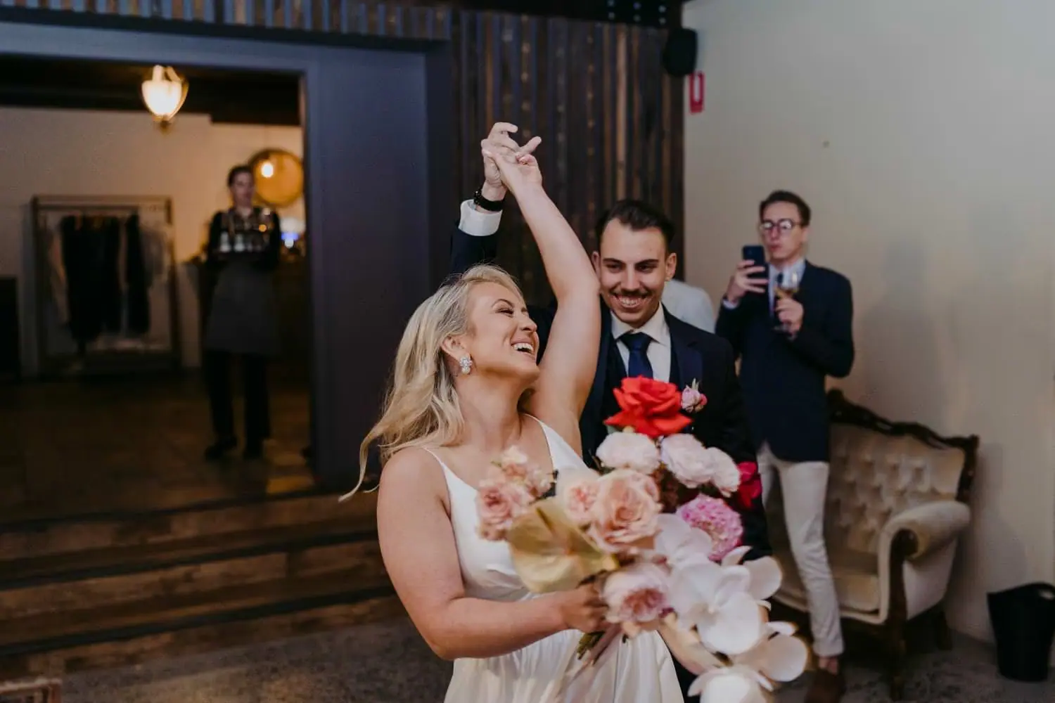 Bride raising her arm as the groom leads her into the reception