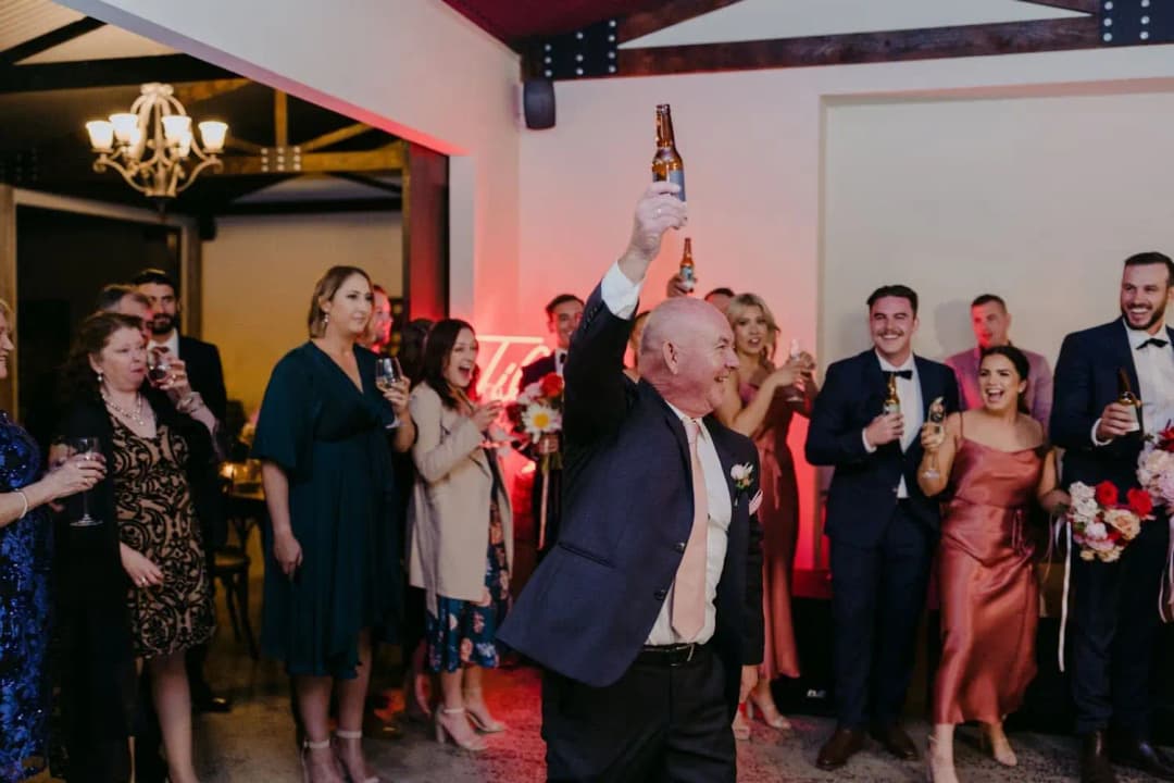 Guest raising a bottle above his head as people cheer at the reception