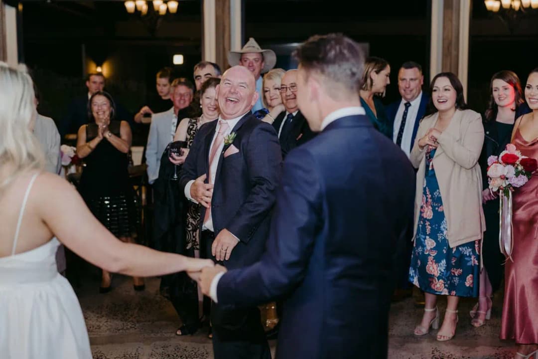 Bride and groom holding hands as a smiling guest dances between them