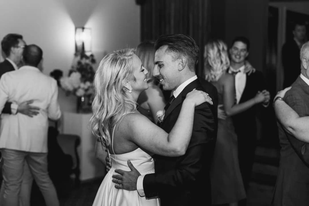Black and white photograph of the bride and groom smiling closely together while dancing